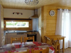 A compact kitchen with a window, a sink, and a stove. There is a wooden table and chairs in the dining area.