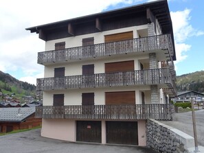 A multi-story building with balconies, a stone facade, and a parking area.