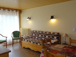 A cozy room with a wooden sofa, a green chair, a wooden table, and a bed with a quilt.