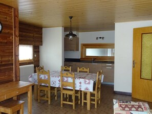 A cozy kitchen with wooden cabinets, a dining table with chairs, and a hanging light fixture.