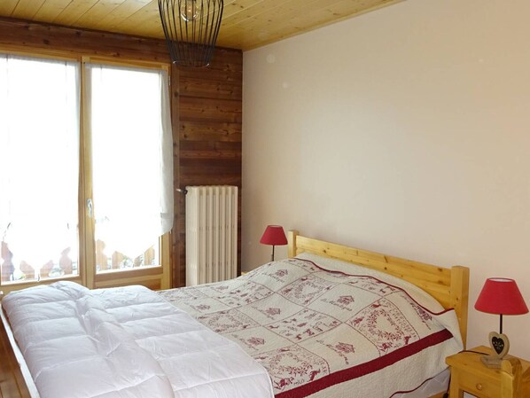 A wooden cabin bedroom with a large bed, two bedside lamps, and a window with curtains.