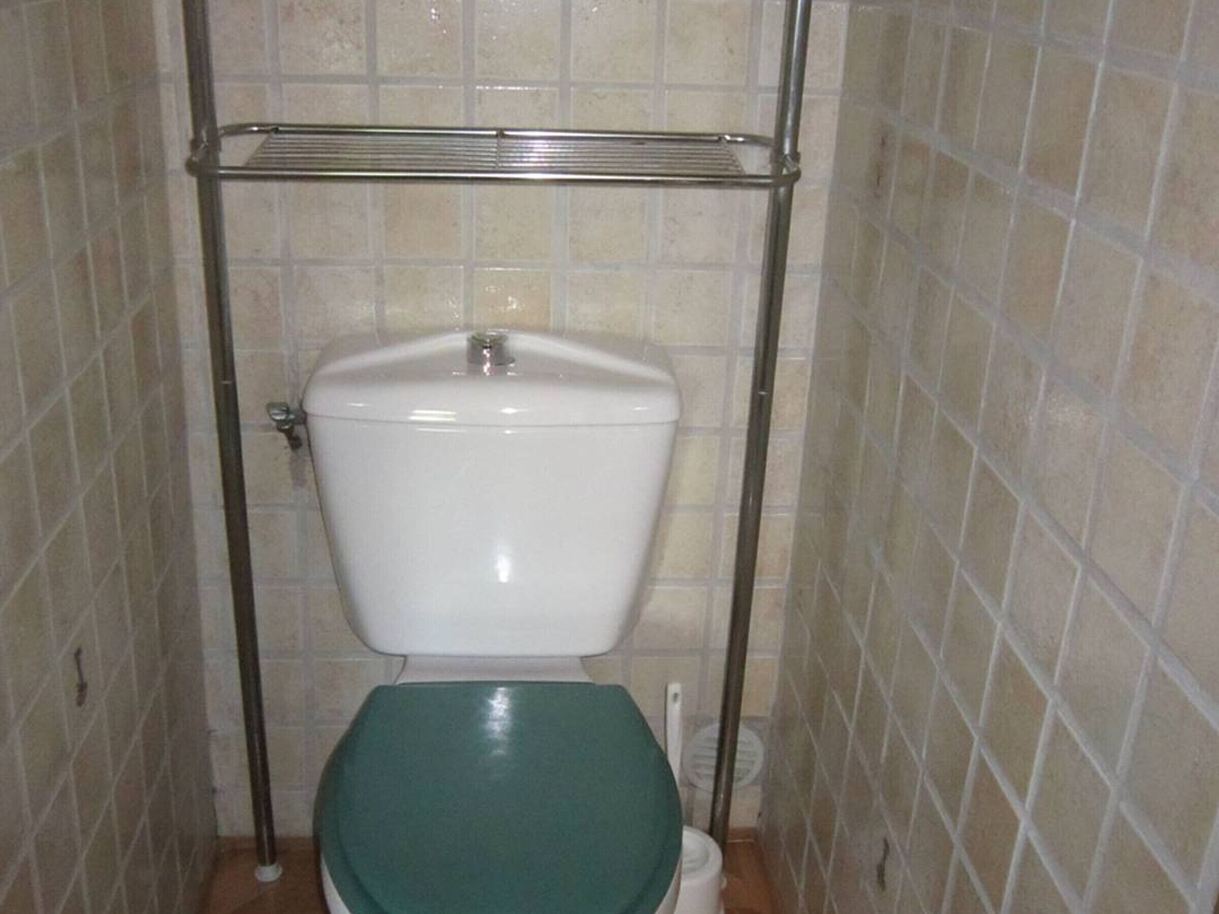 A small, tiled bathroom with a toilet and a metal shelf above it.