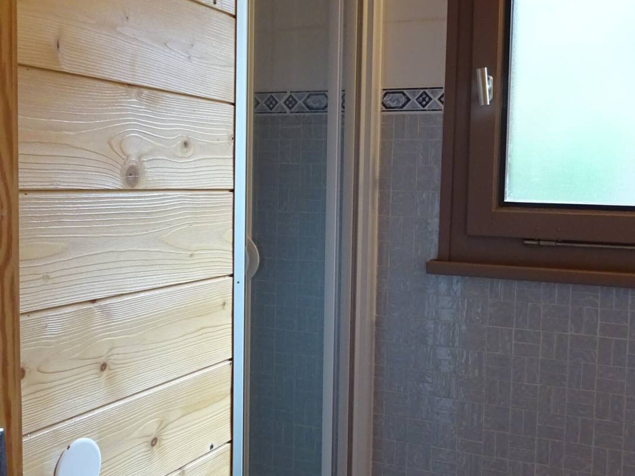 A wooden wall with a white door, a tiled shower area, and a window with a view.