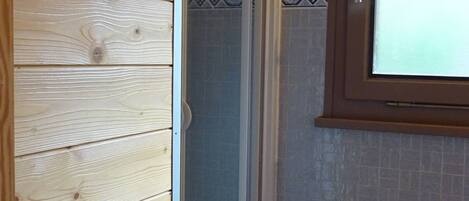 A wooden wall with a white door, a tiled shower area, and a window with a view.