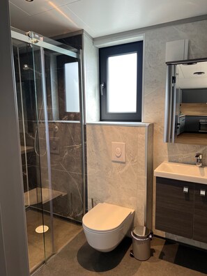 A modern bathroom with a glass-enclosed shower, a toilet, a sink, and a window above the sink.