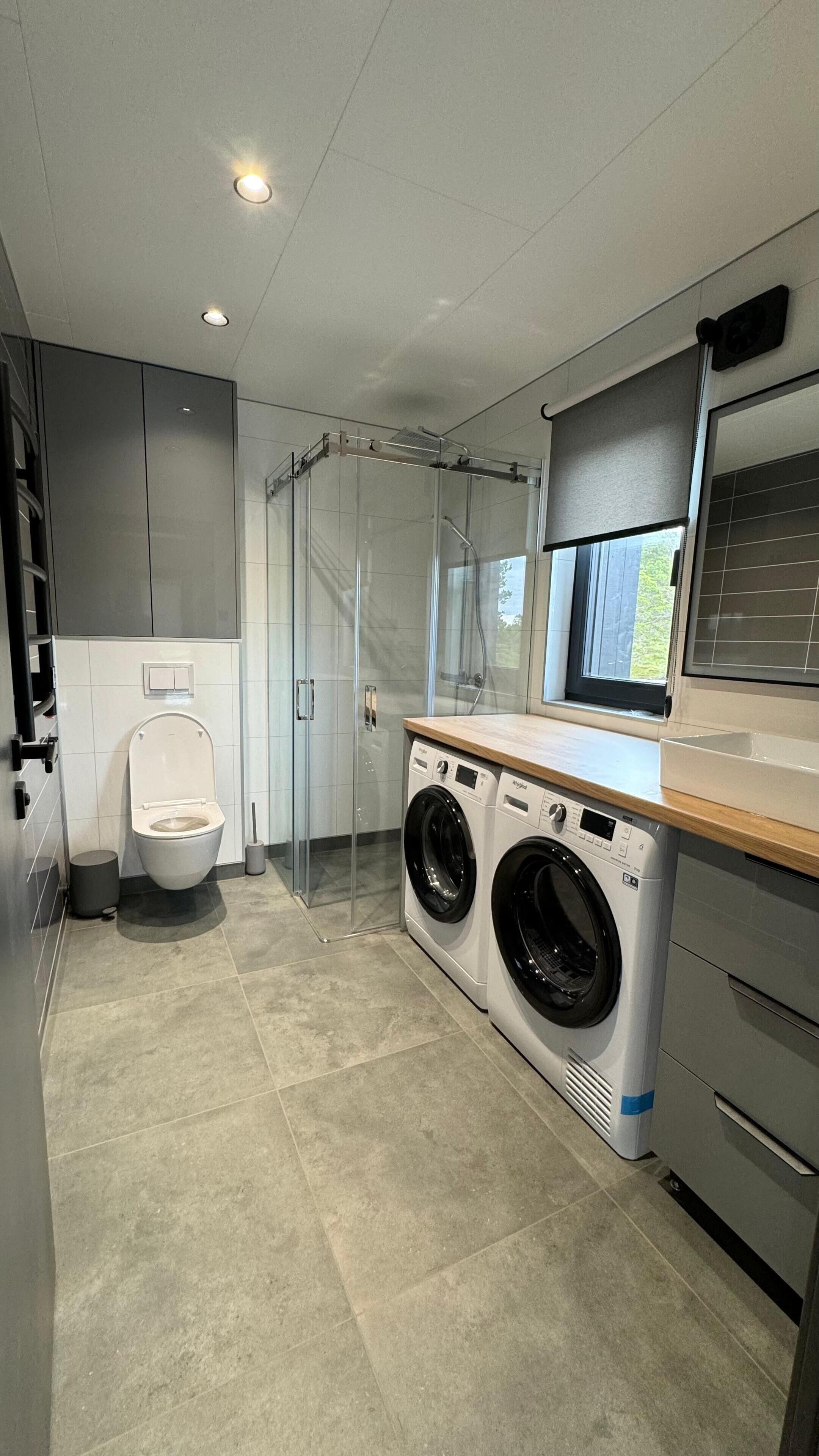 Een moderne wasserij met een wasmachine, droger en een douchecabine met glazen wanden.