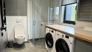 Een moderne wasserij met een wasmachine, droger en een douchecabine met glazen wanden.