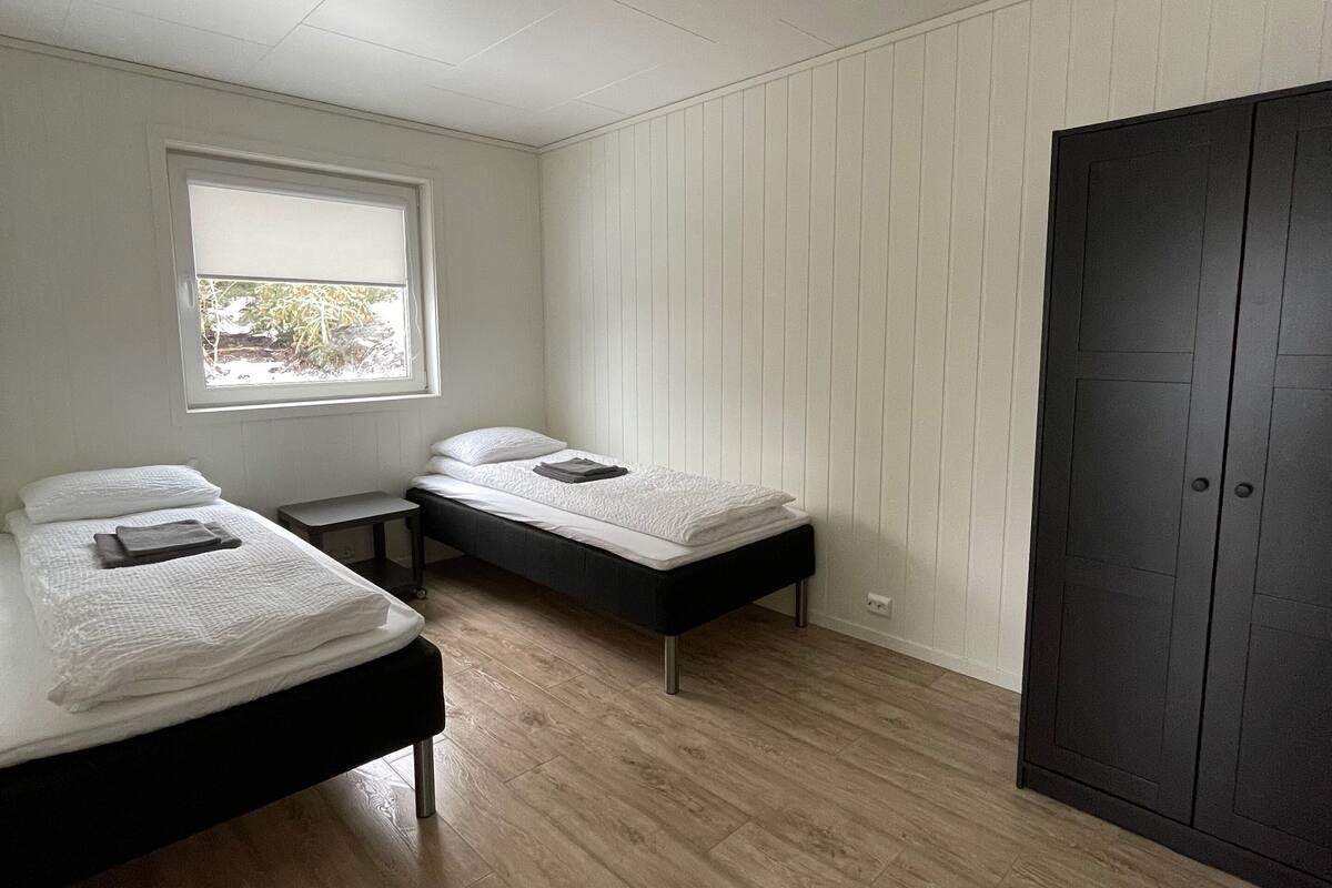 A room with two beds, a window, a wardrobe, and a ceiling light.