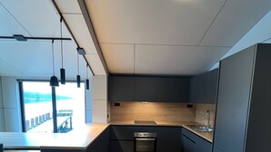 Eine moderne Küche mit einer zentralen Kochinsel, integriertem Backofen und Blick auf ein Gewässer durch große Fenster.