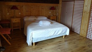 Une chambre dans une cabane en bois, avec un lit, deux tables de chevet, un fauteuil à carreaux rouges et un mur à carreaux.