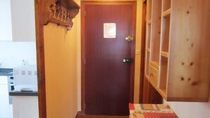 A narrow hallway with a wooden door, a small mat at the entrance, and a table with a patterned tablecloth. - Cozy 2-Room Apartment for 5, South-Facing Balcony, Near Shops and Slopes, Garage Included (Les Gets)