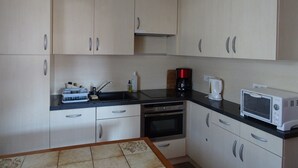 A kitchen with light-colored cabinets, a black countertop, a coffee maker, a microwave, and a stove. - Cozy 2-Room Apartment for 5, South-Facing Balcony, Near Shops and Slopes, Garage Included (Les Gets)