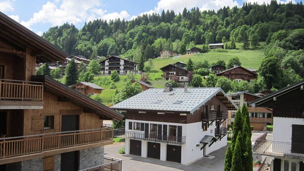 A multi-story building with balconies, a central courtyard, and a view of a forested hillside. - Cozy 2-Room Apartment for 5, South-Facing Balcony, Near Shops and Slopes, Garage Included (Les Gets)