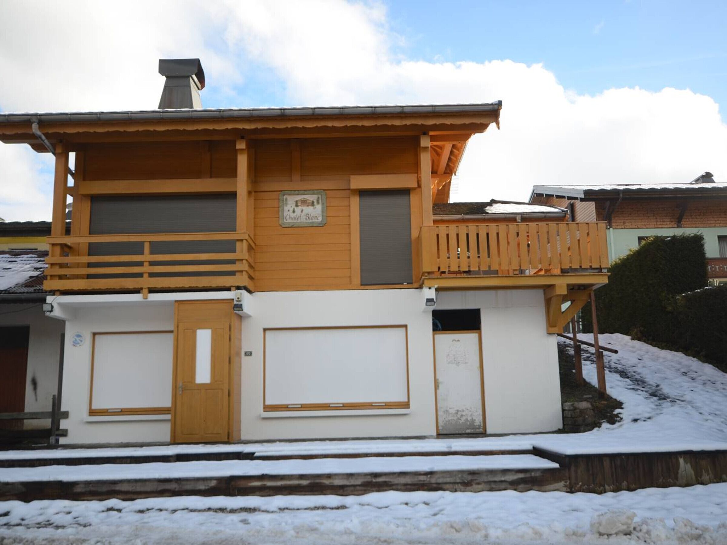 A two-story building with a wooden balcony, a garage door, and a sign that reads "Chalet Blanc".