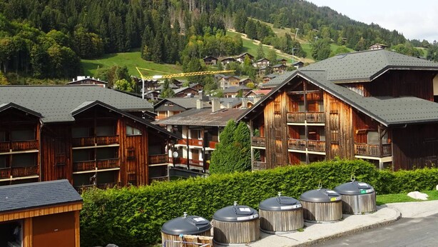 A cluster of wooden cabins with balconies, set against a backdrop of a forested hillside. - Les Gets - Duplex 5 rooms, 10 pers, near slopes, terrace, parking (Les Gets)