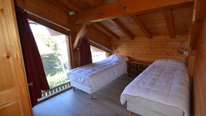 A wooden cabin with two beds, a window with red curtains, and a view of greenery outside. - Les Gets - Duplex 5 rooms, 10 pers, near slopes, terrace, parking (Les Gets)