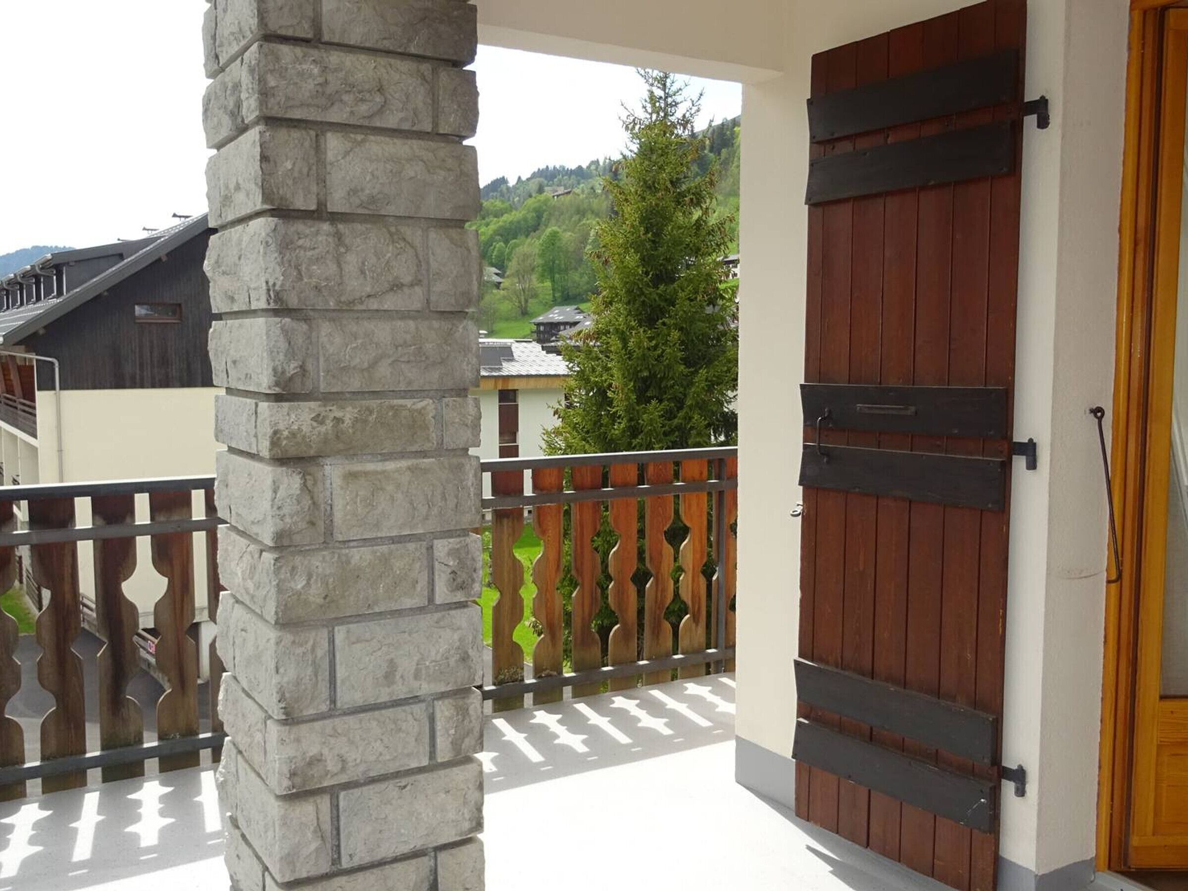 Ein Balkon mit einer Steinsäule, einem Holzzaun und einer Holztür mit schwarzem Griff.