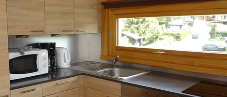 Una cocina con armarios de madera, microondas, cafetera, pileta y lavavajillas.