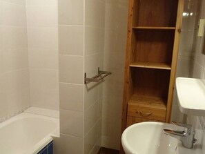 A bathroom with a bathtub, a wooden shelf, and a sink.
