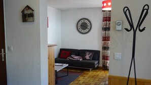 A living room with a sofa, a wall clock, and a red and white patterned curtain. - Les Gets Duplex 3-Room - 6 Pax, Comfortable, Garage (Les Gets)