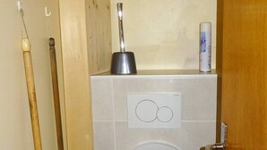 Un baño con un inodoro, un desatascador y dos cepillos de limpieza.