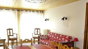 Un comedor con una mesa redonda, sillas de madera, un sofá rojo y dos lámparas fijadas a la pared.