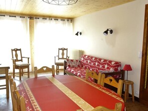 A dining area with a round table, wooden chairs, a red sofa, and two wall-mounted lamps.
