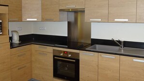 Cocina moderna con armarios de madera, extractor de acero inoxidable, horno empotrado y encimera negra.
