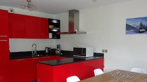 Une cuisine moderne avec des meubles de rangement rouges, un plan de travail noir et une table à manger en bois.