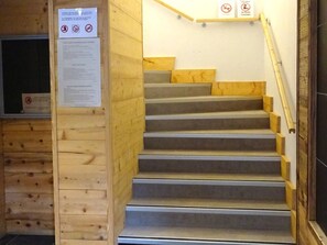 A wooden staircase with a handrail, a wooden wall panel, and a sign with no smoking and no pets symbols. - Modern 3-Room Apartment, 5 People, Garage, Near Slopes, WiFi (Les Gets)
