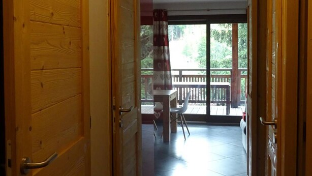 Une porte en bois donnant sur un balcon d’où l’on peut admirer les arbres et qui est agrémenté d’une balustrade.