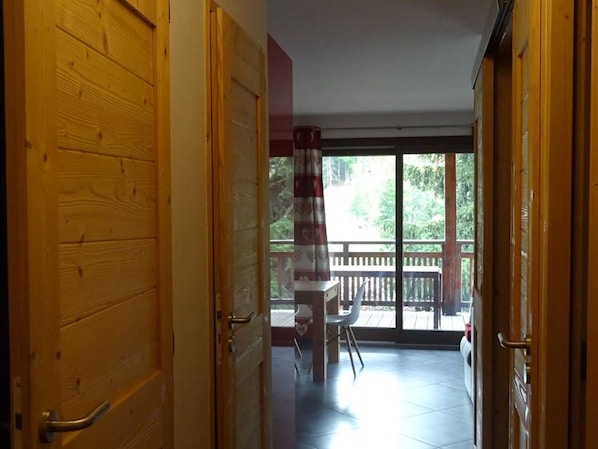 A wooden door leading to a balcony with a view of trees and a railing.