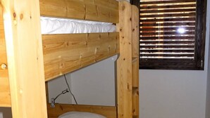 Un lit superposé avec une structure en bois et une literie blanche, une fenêtre avec des stores et un mur uni.
