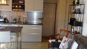 Une cuisine compacte avec un coin repas, un plancher en bois et un coin salon confortable avec un canapé et un fauteuil.