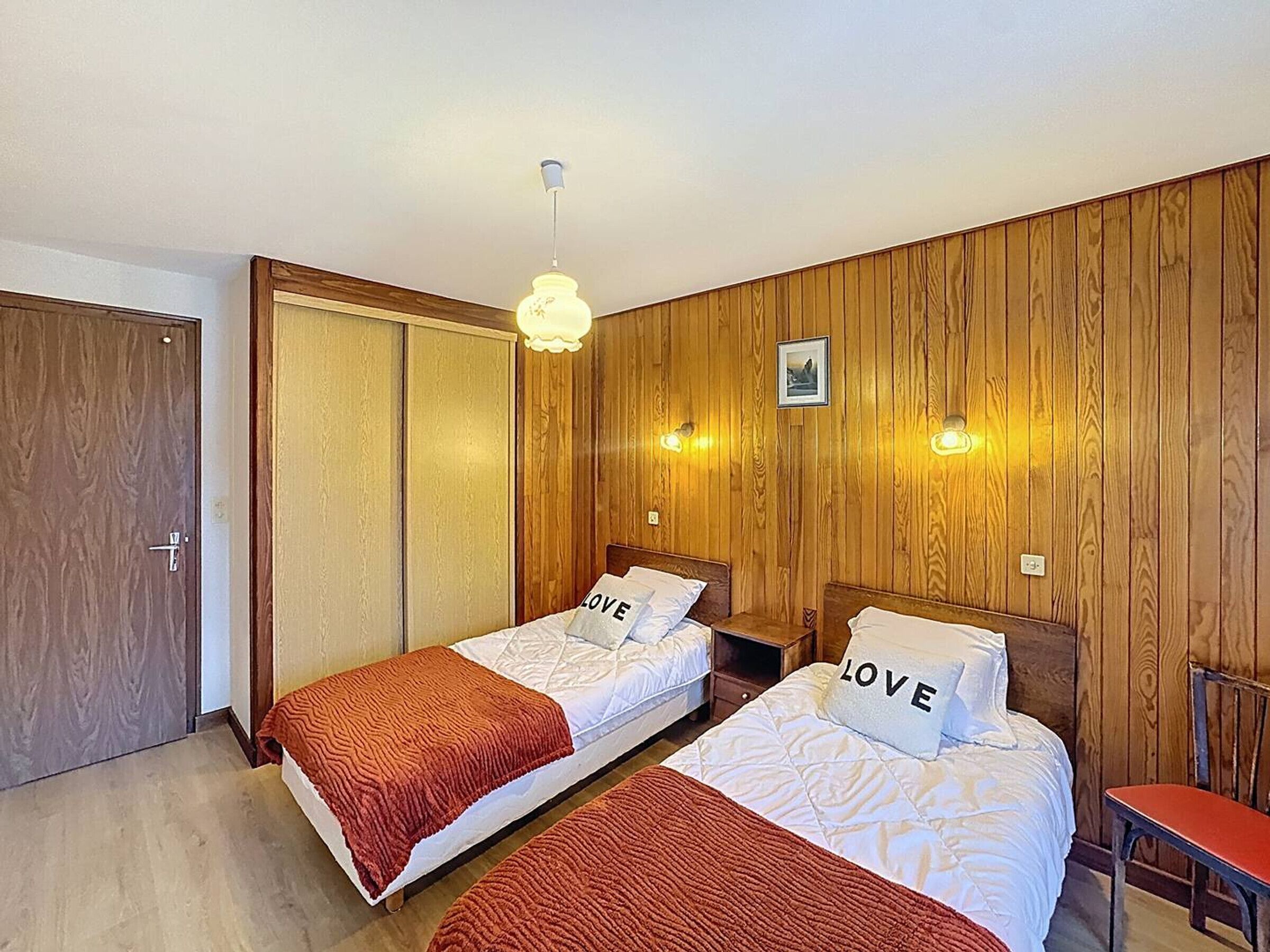 A hotel room with two beds, wooden panel walls, a ceiling light, and a small picture on the wall.