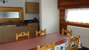 A kitchen with wooden cabinets, a black countertop, and a red and white checkered tablecloth-covered dining table with four chairs. - Spacious 2-BR Apartment for 7 with WiFi, Central Heating, and Parking - Les Gets (Les Gets)