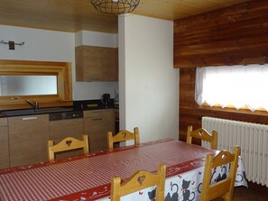 A kitchen with wooden cabinets, a black countertop, and a red and white checkered tablecloth-covered dining table with four chairs. - Spacious 2-BR Apartment for 7 with WiFi, Central Heating, and Parking - Les Gets (Les Gets)