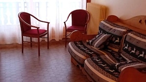 A room with a sofa and two chairs, a radiator, and a view of the outside through a window with sheer curtains. - Spacious 2-BR Apartment for 7 with WiFi, Central Heating, and Parking - Les Gets (Les Gets)