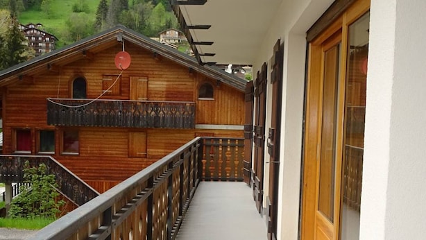 A wooden chalet with a balcony, a satellite dish, and a view of a green valley. - Spacious 2-BR Apartment for 7 with WiFi, Central Heating, and Parking - Les Gets (Les Gets)