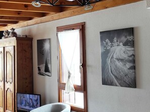 Una habitación con techo de madera, televisor, mueble aparador y dos cuadros en la pared.
