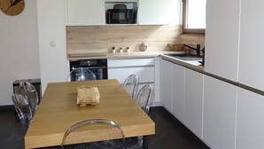 Una cocina moderna con armarios blancos, encimera de madera, microondas, lavabo y zona de comedor con mesa y sillas de madera.