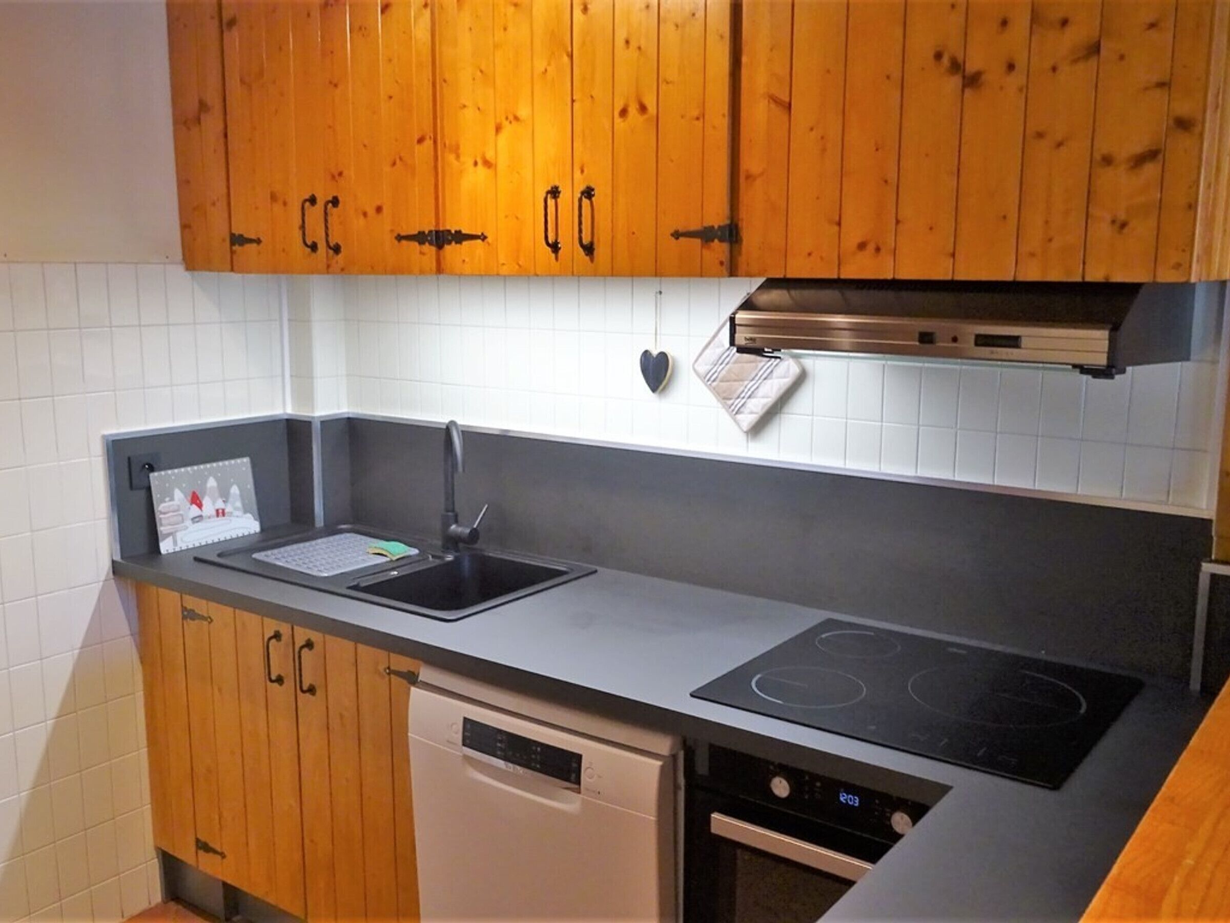 A kitchen with wooden cabinets, a dishwasher, a sink, and an induction cooktop.