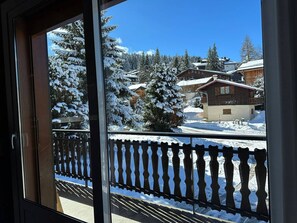 A view from a window with a wooden railing, snow-covered trees, and a building with a red roof.