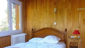 A wooden-paneled room with a bed, a nightstand, and a window. - Spacious 6-Room Duplex, 12 Guests, WiFi, Garage, Close to Slopes - Sheets & Towels Included in Winter (Les Gets)