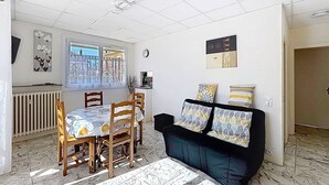Ein Wohnzimmer mit Esstisch, Stühlen, einer Couch mit gemusterten Kissen, einer Heizung und einem Fenster mit Blick.