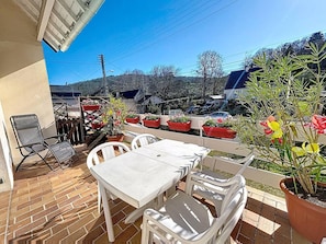 An outdoor patio with white tables and chairs, potted plants, and a view of the surrounding area.