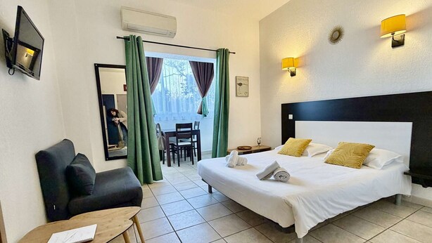 Une chambre d’hôtel avec un lit, un bureau, une chaise, un miroir et une fenêtre avec des rideaux.