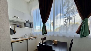 Une cuisine compacte équipée d’un four à micro-ondes, d’une cuisinière, d’un évier et d’un petit réfrigérateur. On y trouve une table à manger avec des chaises, ainsi qu’une fenêtre avec des rideaux.