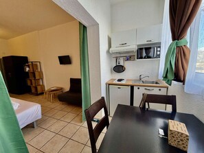 Quarto de hotel pequeno, com cozinha compacta, cama, mesa e televisão.