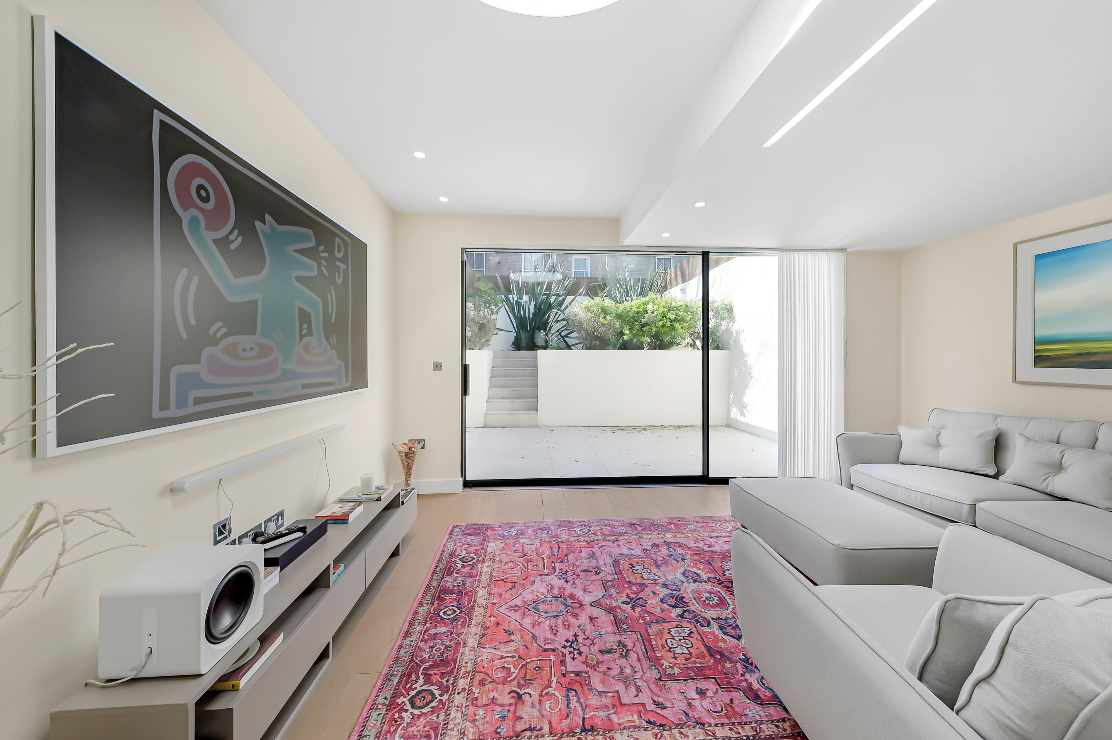 A modern living room with a large flat-screen TV, a grey sofa, a patterned rug, and a sliding glass door leading to a balcony.